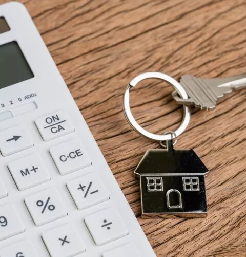 Touche d'accueil avec porte-clés en forme de maison ou porte-clés avec calculatrice blanche sur une table en bois, utilisé pour calculer les mensualités d'un prêt immobilier ou pour acheter et vendre des biens immobiliers.