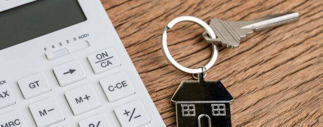 Touche d'accueil avec porte-clés en forme de maison ou porte-clés avec calculatrice blanche sur une table en bois, utilisé pour calculer les mensualités d'un prêt immobilier ou pour acheter et vendre des biens immobiliers.